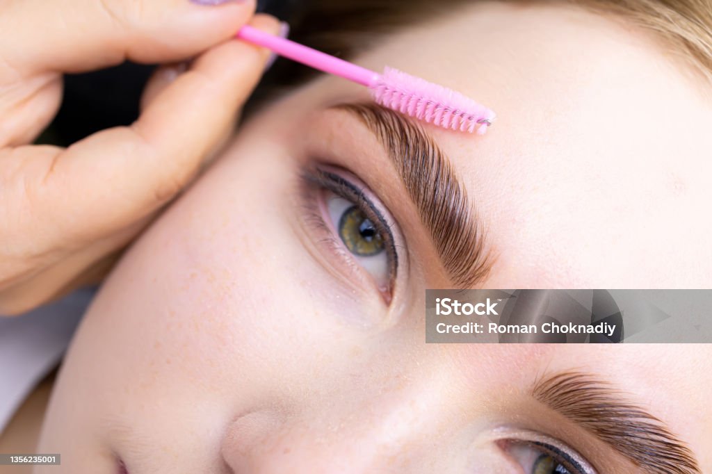 Eyebrow lamination blonde model eyebrow lamination macro photography of the model's hairs the master combs the eyebrow hairs with a pink brush after the procedure long-term styling and lamination Eyebrow Stock Photo