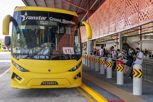 Singapore, Singapore - November 29, 2021: A row of people wait at Woodlands Temporary Bus Interchange to board a coach bus headed for Johor Bahru in Malaysia. The buses were travelling on the first day of a Vaccinated Travel Lane (VTL) scheme launched by the two countries.