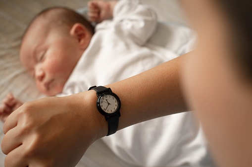 A mother looking at her watch monitoring the time for her baby to eat sleep and wake.