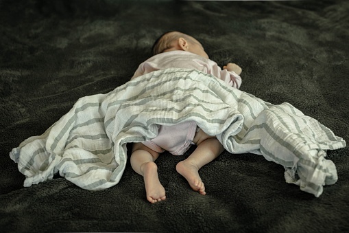 Un bebé durmiendo en posición peligrosa sobre el estómago y la manta suelta. Síndrome del lactante repentino. photo