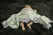 A infant baby sleeping in dangerous position on stomach and loose blanket. Sudden Infant Syndrome.