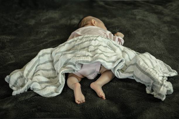 A infant baby sleeping in dangerous position on stomach and loose blanket. Sudden Infant Syndrome. A newborn baby laying on her stomach and with loose bedding. SIDS awareness. dead stock pictures, royalty-free photos & images