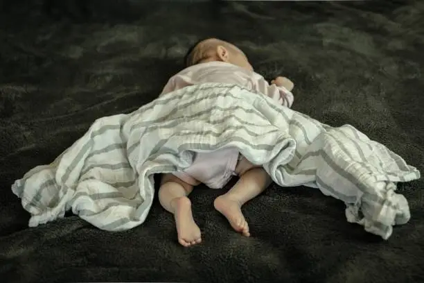 A newborn baby laying on her stomach and with loose bedding. SIDS awareness.