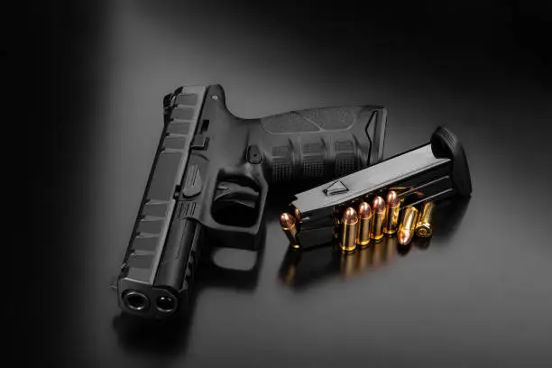 Black modern gun and ammunition for it on a dark reflective surface. Short-barreled weapons for sports and self-defense. Armament for police units, special forces and the army. Black background