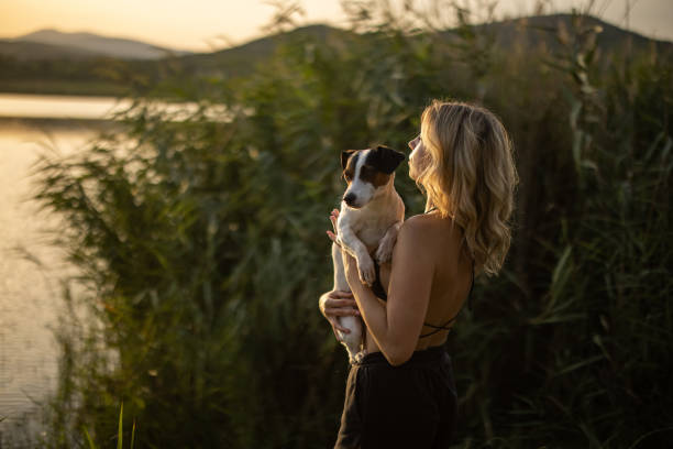 istock Young woman carrying her dog while standing on lakeshore 1356238564