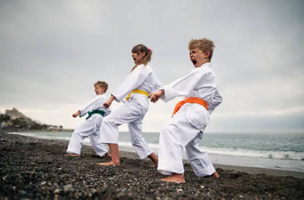 Three kids practicing karate on the beach. The kids are wearing karategi and karate belts.