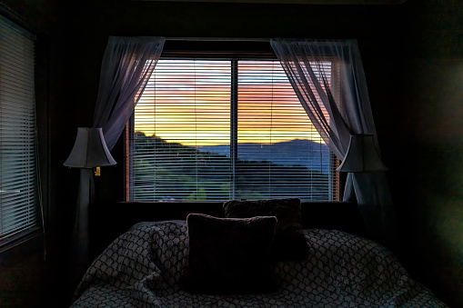 Sugar Mountain, North Carolina view through window of Blue Ridge mountains at sunset from bedroom room of house home or apartment with curtains and bed