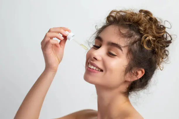 Photo of Shot of beautiful woman applying serum to her clean face skin against a face wrinkles