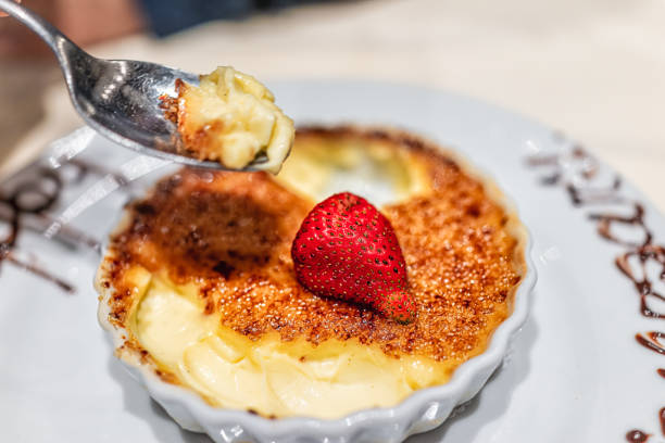 makro-nahaufnahme des handlöffels, der crème brulee-dessertteller mit verbrannter zuckerspitze und erdbeere auf kruste und handgemachter schokoladensauce zum glücklichen jubiläum isst - burnt sugar stock-fotos und bilder