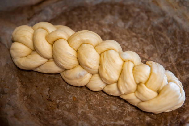 Fresh homemade large loaf of yellow Challah bread raw dough on parchment paper braided shape rising before baking as traditional Jewish Shabbat bread