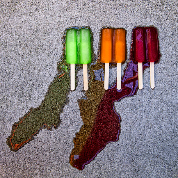 Three Melting Multicolored Popsicles on Cement This is a photograph of 3 popsicles next to each other melting on the ground. This image could relate to summertime heat wave or global warming flavored ice photos stock pictures, royalty-free photos & images