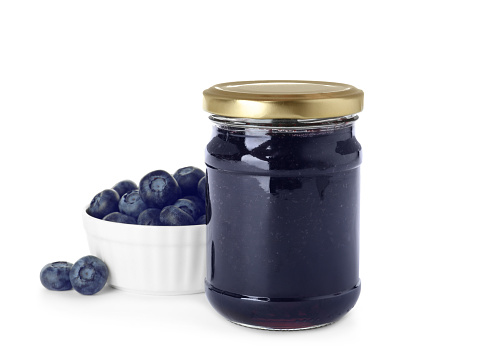 Jar of blueberry jam and fresh berries on white background