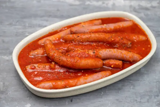 fresh sausages with tomato sauce on the dish on ceramic background