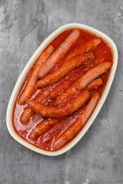 fresh sausages with tomato sauce on the dish on ceramic background