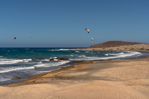 View on long sandy beach of El Medano surfing beach with many surfers in the air.