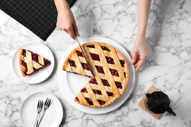 istock Woman cutting tasty cherry pie at white marble table, top view 1356248196