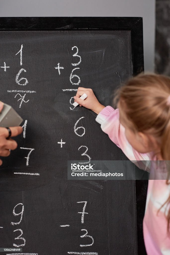 Girl writing down math solution on blackboard while counting numbers at school lesson Counting numbers at school lesson Number Stock Photo