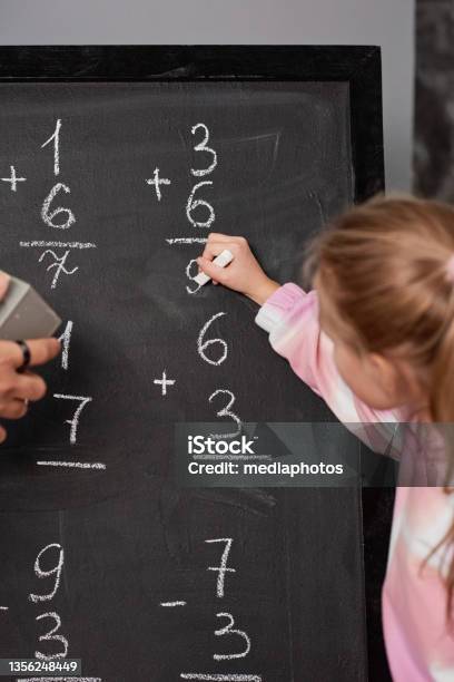 Girl Writing Down Math Solution On Blackboard While Counting Numbers At School Lesson Stock Photo - Download Image Now