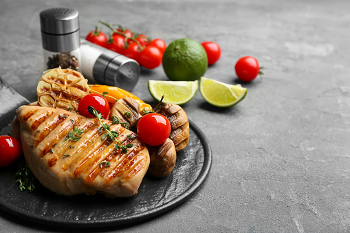 Tasty grilled chicken fillet with tomatoes and thyme on grey table, closeup