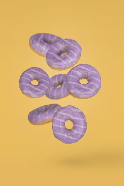 istock Purple decorated doughnuts with blueberries in motion falling or flying on yellow background. 1356253150