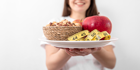 Young woman with a plate of apples and hazelnuts on a white background, the concept of weight loss, healthy eating.