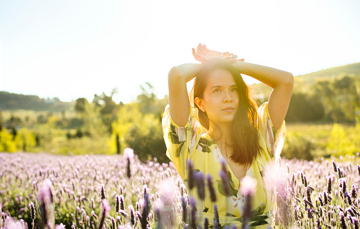Carefree young woman standing alone outside in a field of lavender on a sunny afternoon in the summertime