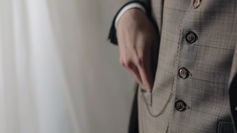 The man holds a watch on a chain in his hand and after checking the time puts it in his pocket. Close-up shooting