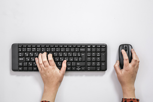Female hands use keyboard and mouse on white background, flat lay.