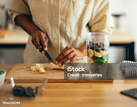 istock Close Up of Woman Hands Cutting Banana on a Cutting Board 1356258289