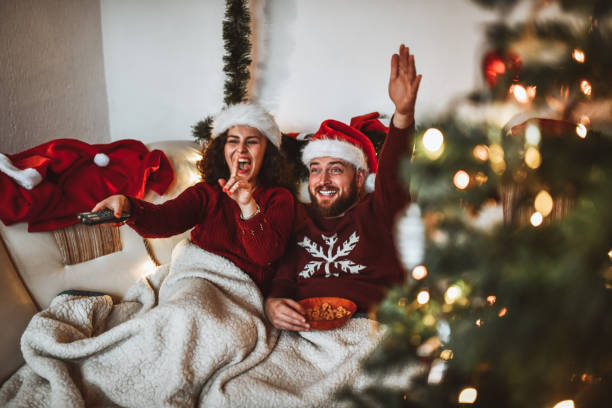 smiling couple with santa hats celebrating christmas by eating snacks and watching tv - remote television movie box imagens e fotografias de stock