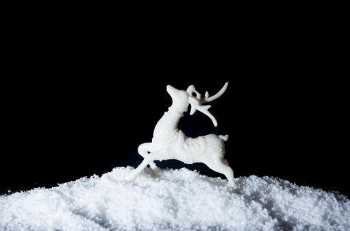 Reindeer in snow on dark black background. Christmas tree decoration toy. Minimal abstract winter holidays concept. Copy space.