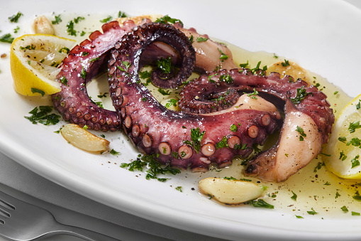 Grilled octopus tentacle on a wooden cut board served with shrimps, green beans, burnt onion and potatoes isolated with clipping path. Delicious barbecue seafood dish with fresh greens top view