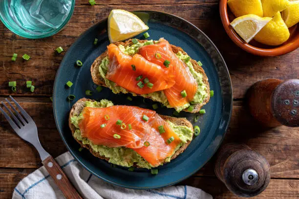 Delicious avocado and smoked salmon toasts on a rustic wood table top.
