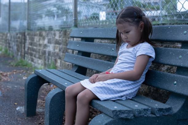 istock A sad little girl sitting alone outside on a bench depressed. 1356272932