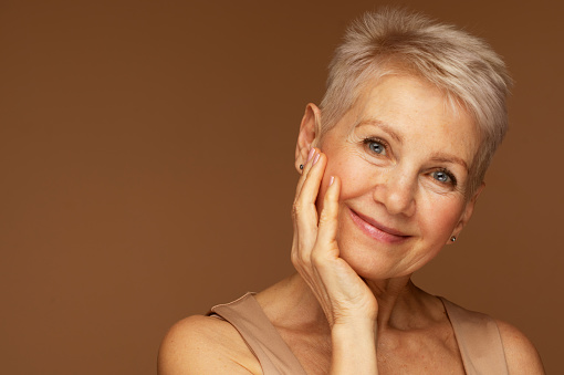 Beauty portrait of mature woman smiling with hand on face. Closeup face of happy senior woman feeling fresh after anti-aging treatment. Smiling beauty looking at camera with perfect skin.