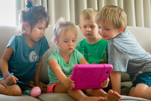 A group of young multiracial kids shariing a eletronic ipad device.