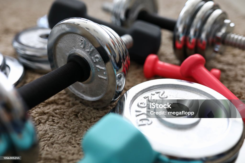 Pile of shiny chrome dumbbells disks lying around grip Pile of shiny chrome dumbbells disks lying around grip at home rug as domestic sport exercises during coronavirus quarantine period close-up Gym Stock Photo