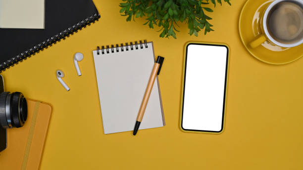 istock Mock up smart phone, notepad, wireless ear phones and coffee cup on yellow background. 1356310278