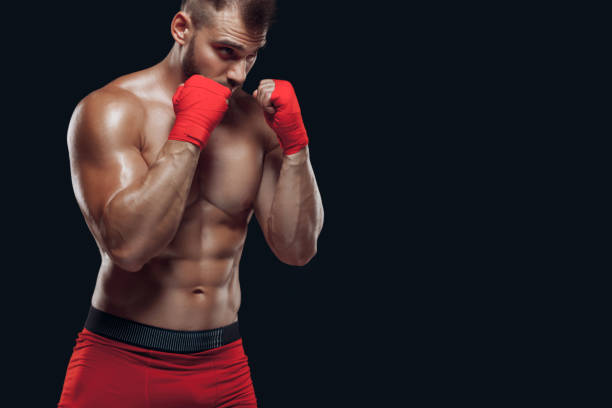 istock Close uo front view of a sporty man in boxing gloves practicing fighting techniques isolated on black background 1356315022