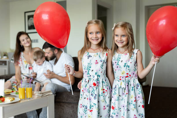 dwie siostry bliźniaczki pozują z balonami w tle rodziny. który je śniadanie w pokoju hotelowym. - hotel room hotel couple domestic room zdjęcia i obrazy z banku zdjęć