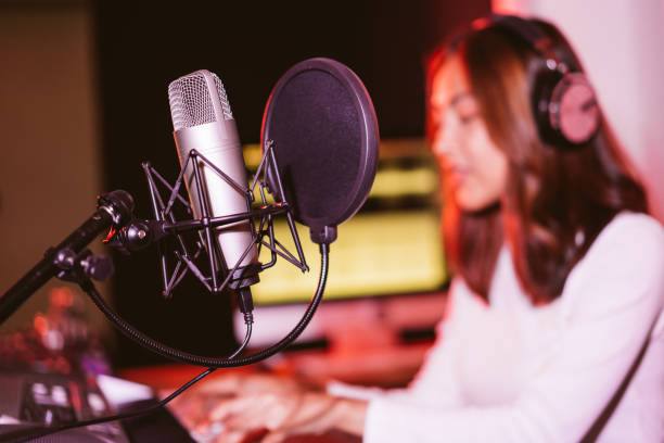 istock Studio microphone and pop shield on the mic in the empty recording studio with blur Asian woman in the background. Performance and show in the music business equipment. 1356321590