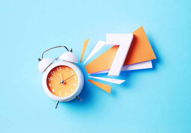 istock Number Seven Sitting Next To A White Alarm Clock On Blue Background 1356324762