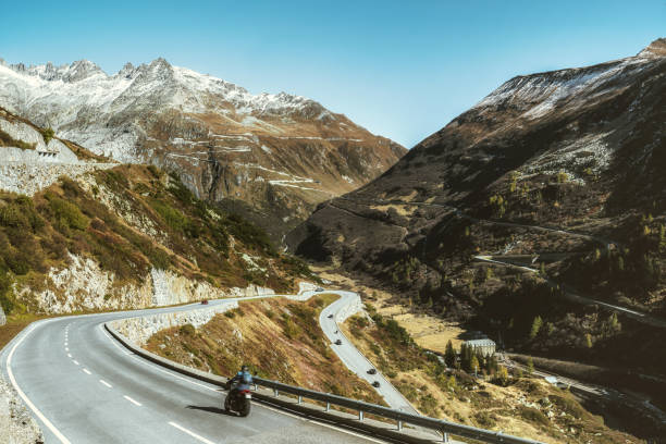 motorbike coming down the grimsel pass road in switzerland single motorbike coming down the winding road of grimsel pass in the swiss alps, the famous furka pass in the background furka pass photos stock pictures, royalty-free photos & images