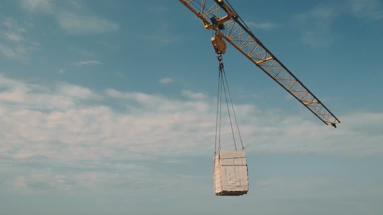 The construction crane lifts the white brick and transfers it to the construction site. A crane on a construction site lifts a load