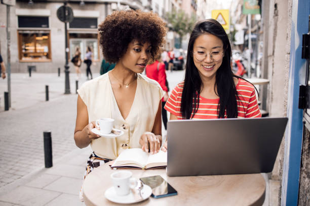 istock Two friends on vacation using laptop at the sidewalk cafe 1356329123