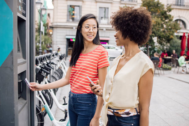 買い物のためにatmからお金を取って�休暇中の2人の若い女性 - spending money adult african ethnicity bag ストックフォトと画像