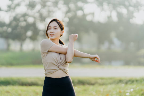 istock Cheerful young Asian woman doing stretching exercise in public park 1356333868