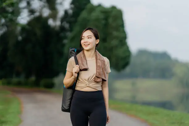 An Asian woman with exercise mat walking in nature, healthy lifestyle and body positive