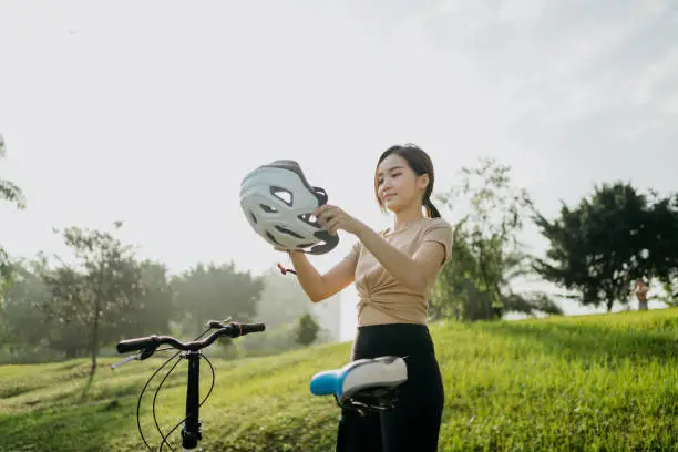 Young woman putting her helmet, preparing for the bike ride at public park.