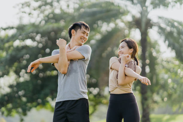 heureux jeune homme et femme qui s’étirent dans le parc - running jogging asian ethnicity women photos et images de collection